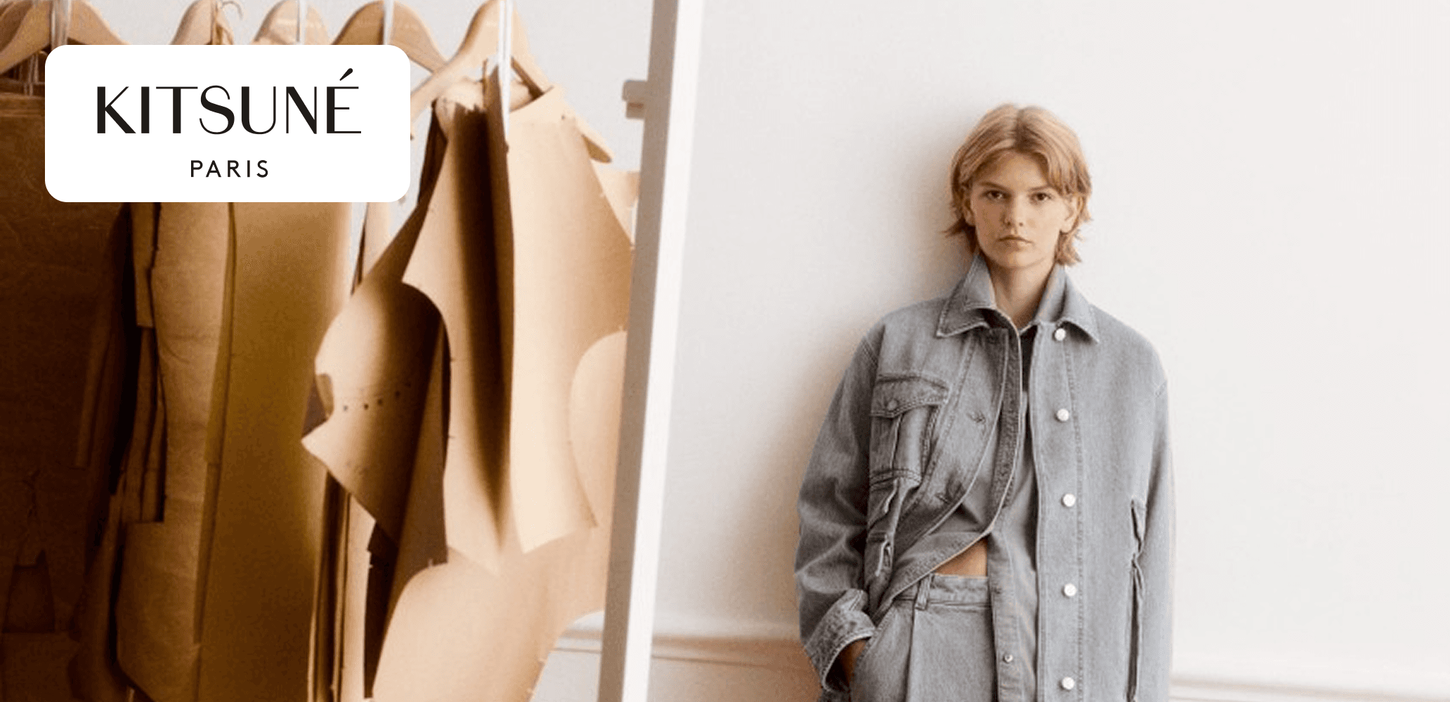 Kitsuné Paris campaign banner showing a person in a light denim outfit standing beside hanging garment patterns in a bright minimal studio.