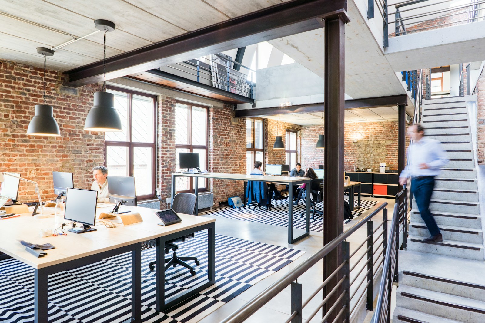 Team desks on a brick-walled loft floor beside a staircase