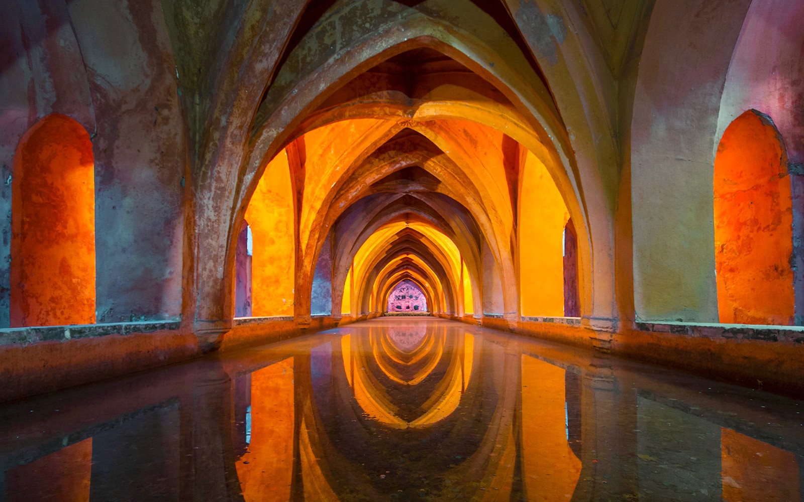 Túnel subterráneo del Real Alcázar de Sevilla con arcos intrincados y reflejos.