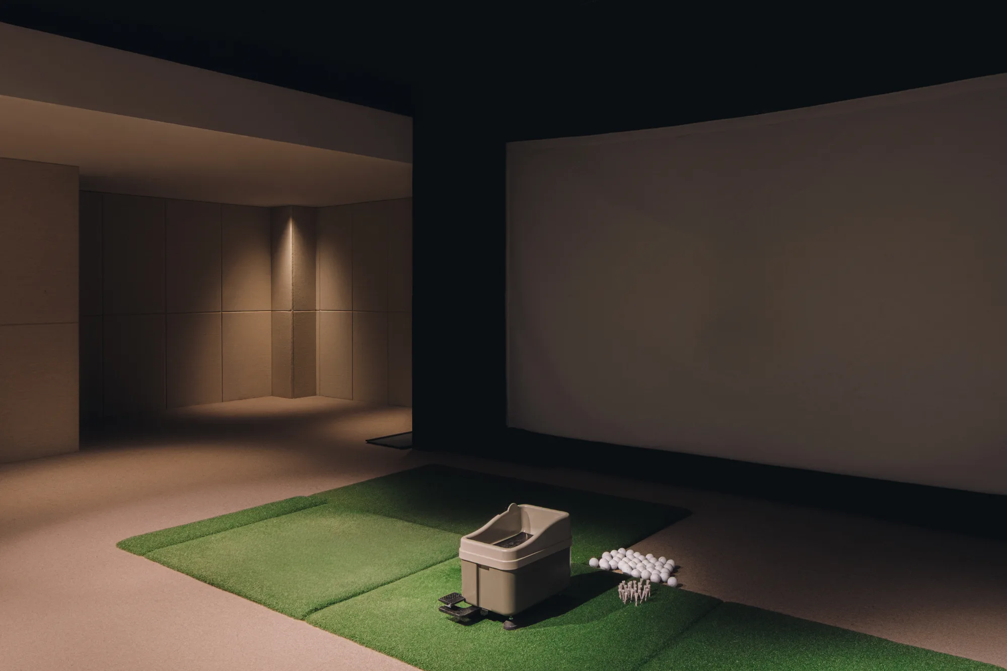 Turf hitting bay and ball dispenser in the darkened PLAYA screen golf room