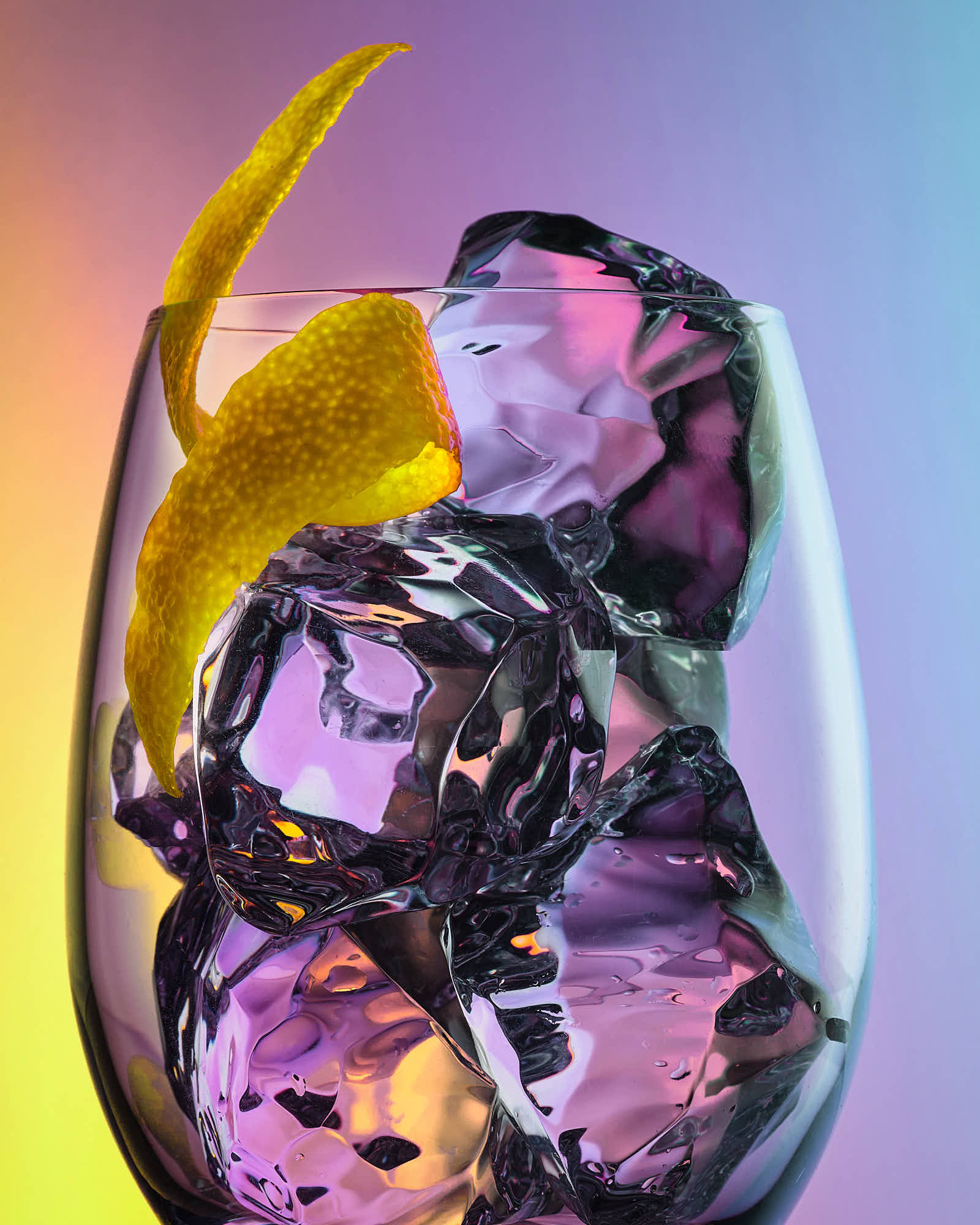 A glass container filled with colorful, swirling ice cubes and lemon twist against a gradient background.
