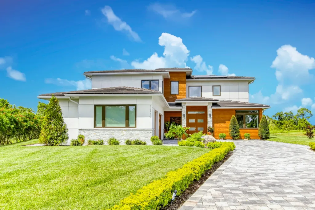 Modern two-story house with white and wood exterior, large windows, and paved driveway.