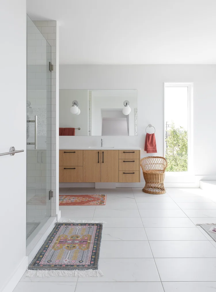 Modern two-story home with large glass windows, warmly lit interiors, and a balcony. Surrounded by trees and a manicured lawn at dusk. Cozy ambiance.