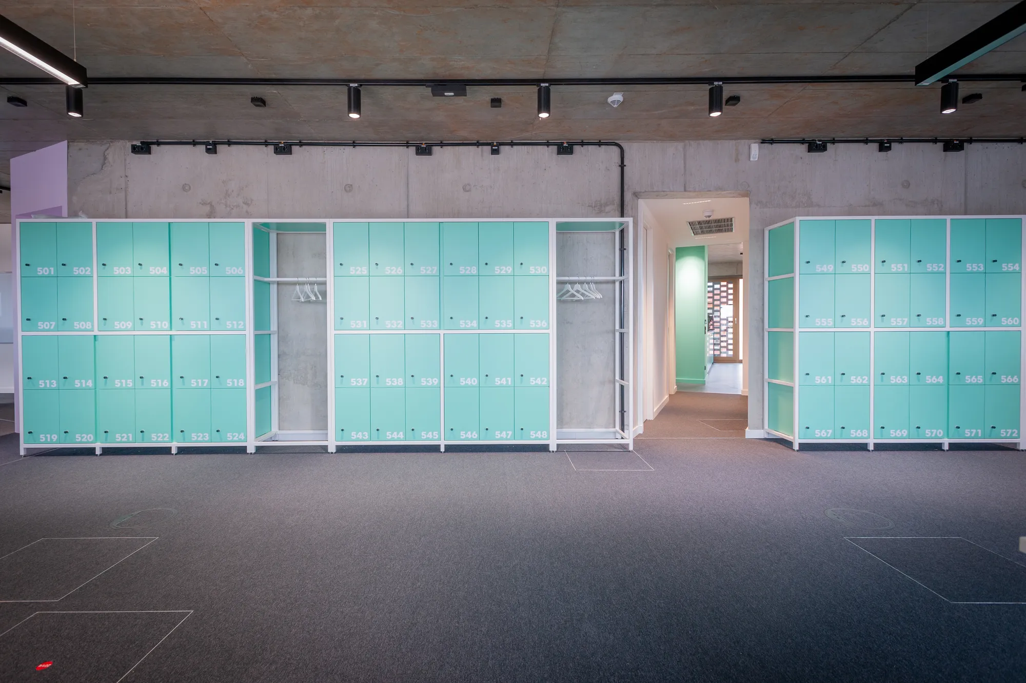 Row of mint-green lockers along a concrete wall in the office corridor.