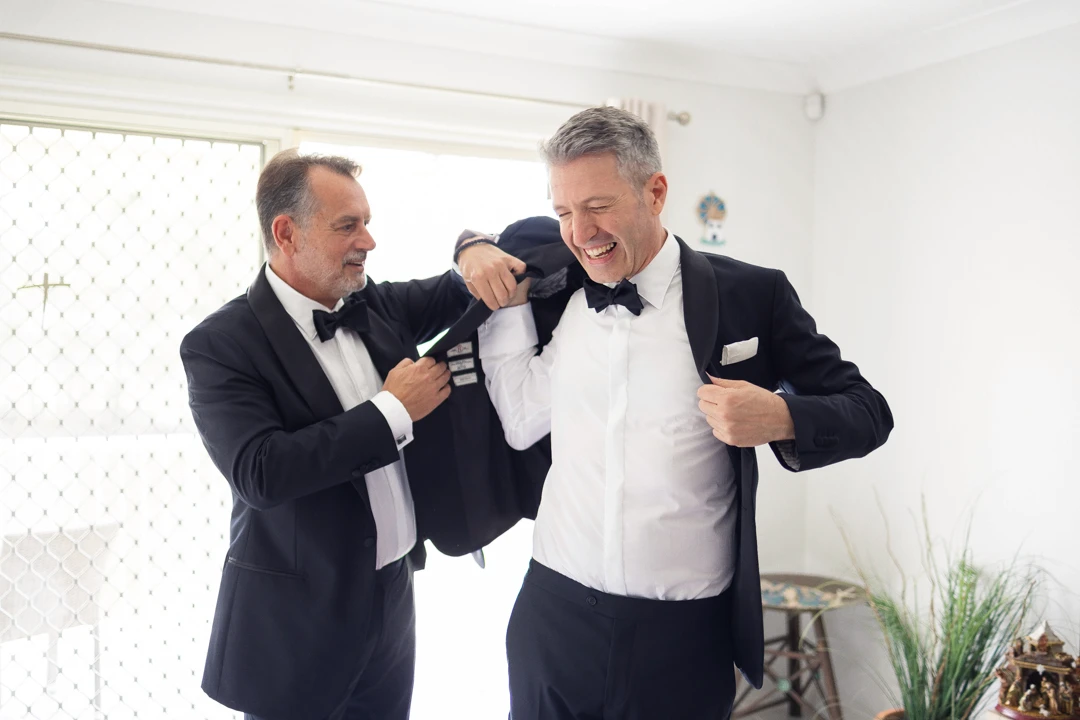 Best man helping groom put on suit jacket
