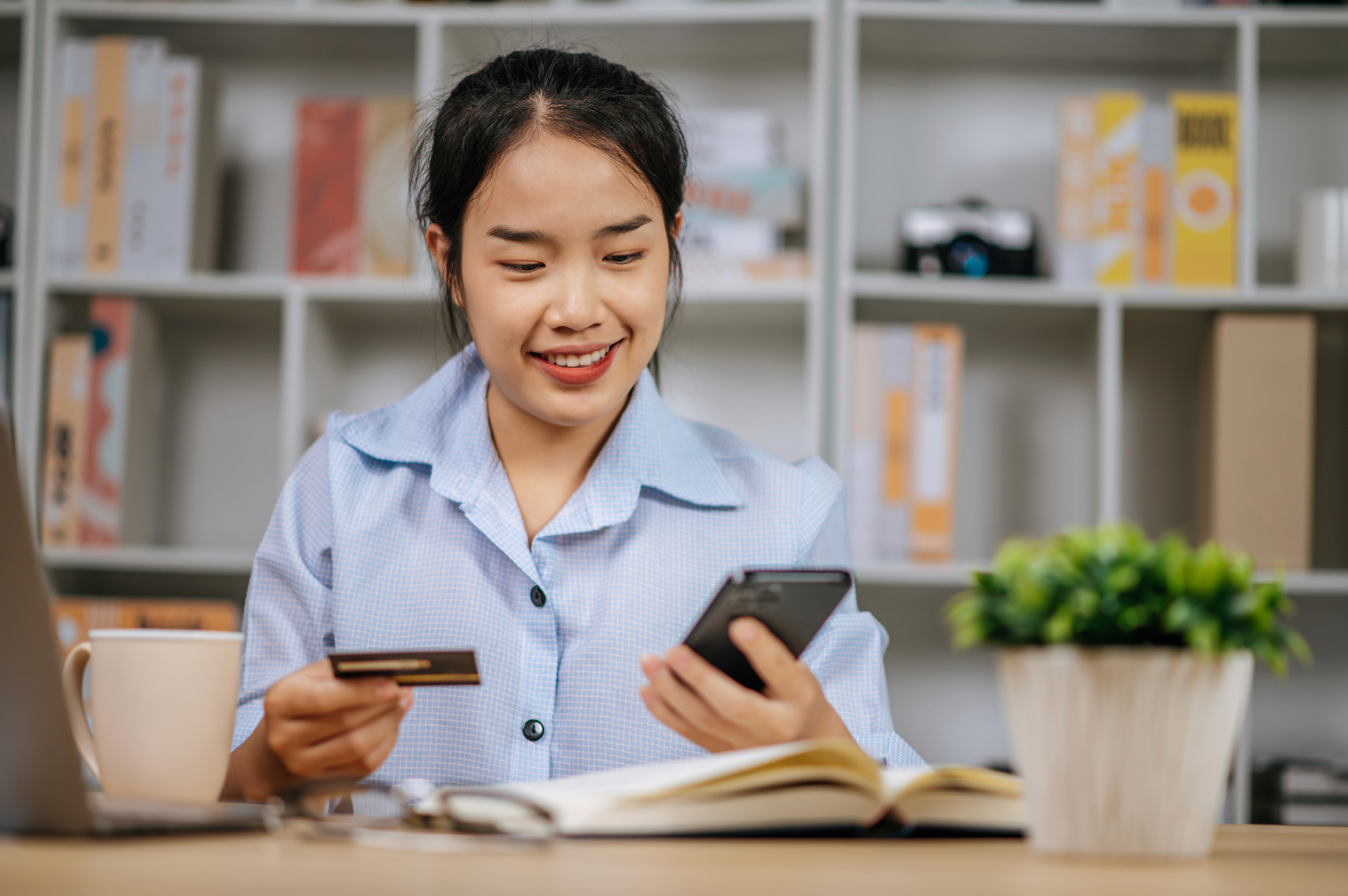 Smiling woman using her smartphone and credit card to access online services for her non-resident account in the UAE.
