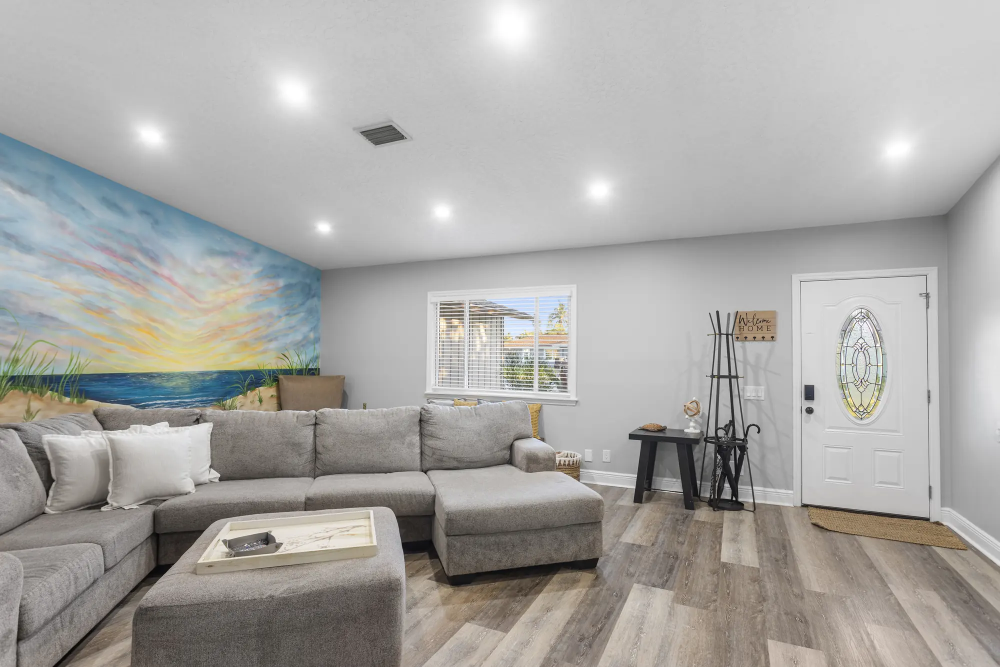 Living room with a gray sectional and a painted sunrise beach mural at Sarasota Beach Bungalow, Bradenton, Florida