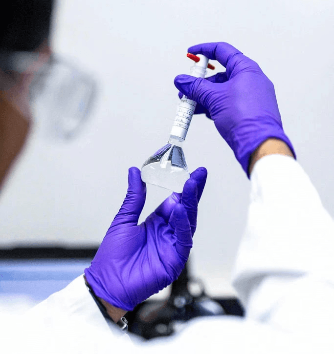 Close-up of a scientist wearing gloves carefully handling a labeled flask in a laboratory.