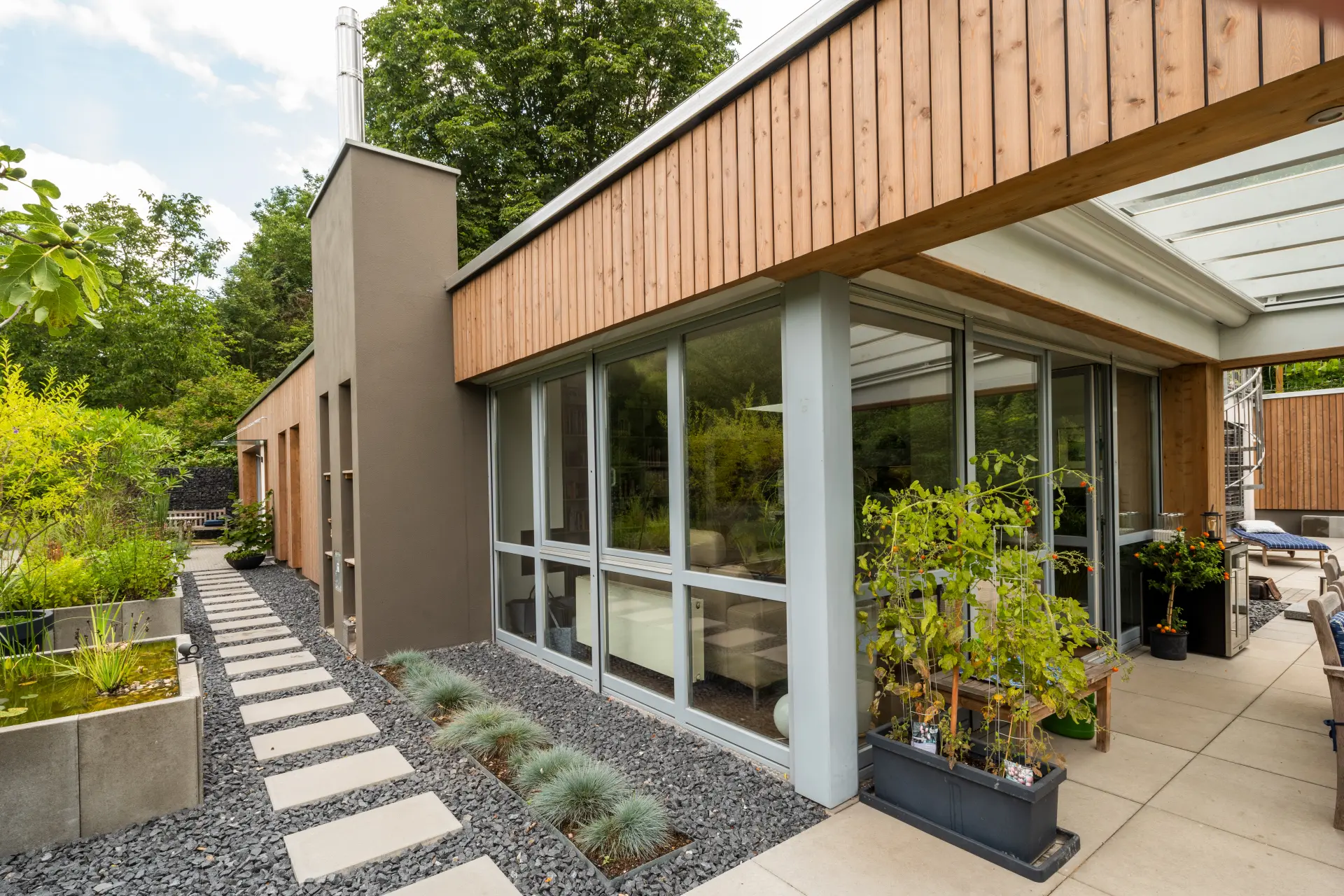 Modernisierte Hausfassade mit Holzverkleidung, Terrasse und bepflanztem Außenbereich