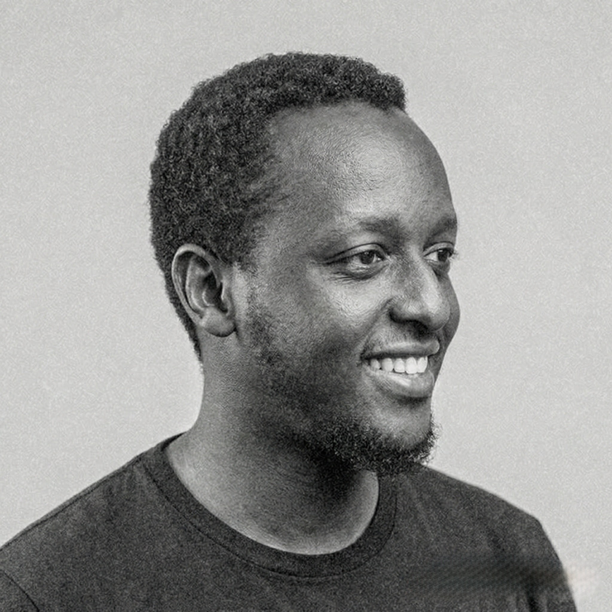 Portrait of a young man with short hair, wearing a dark t-shirt, against a plain background.