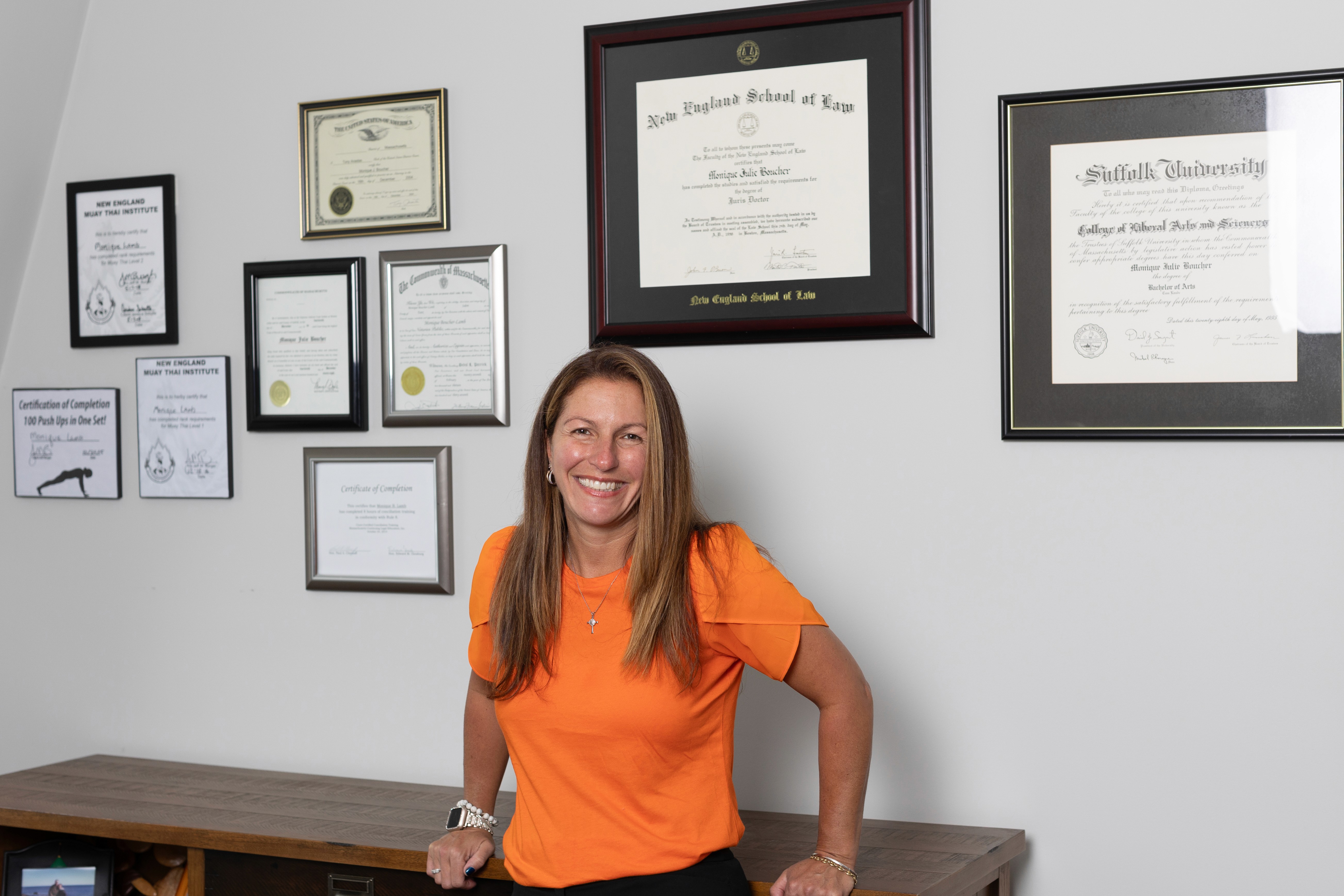 Monique Boucher Lamb, Founding Attorney of Lamb & Lamb, P.C., standing in her Salem, MA law office with diplomas and credentials displayed on the wall behind her