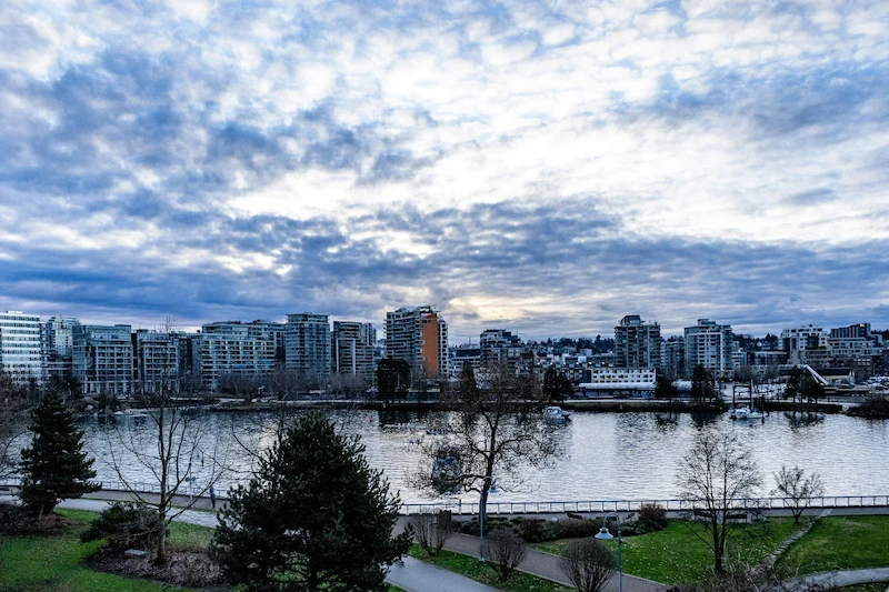 Modern condo skyline across False Creek in Olympic Village, Vancouver, beneath dramatic clouds.