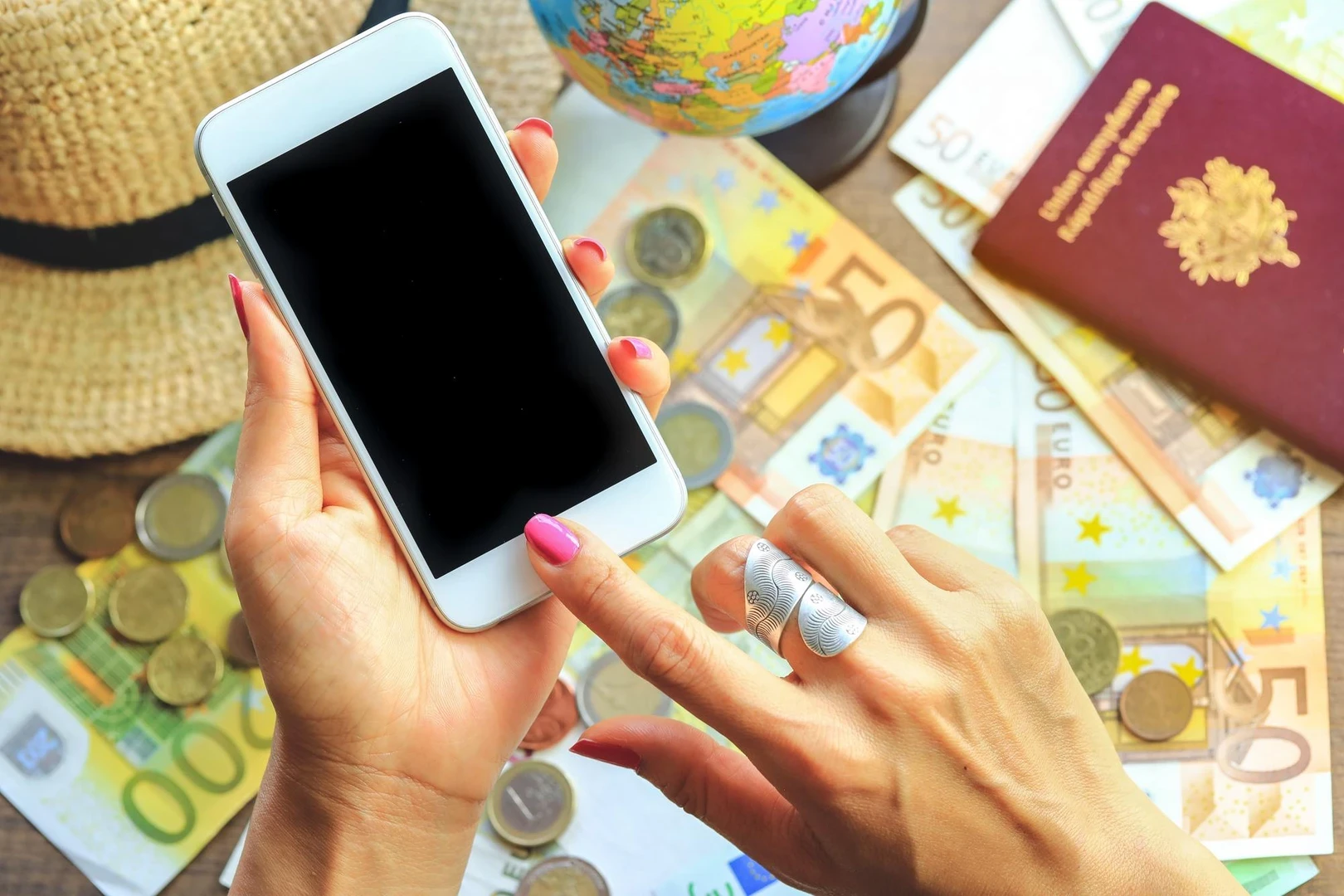 Cropped hand of woman using mobile phone against currency on table