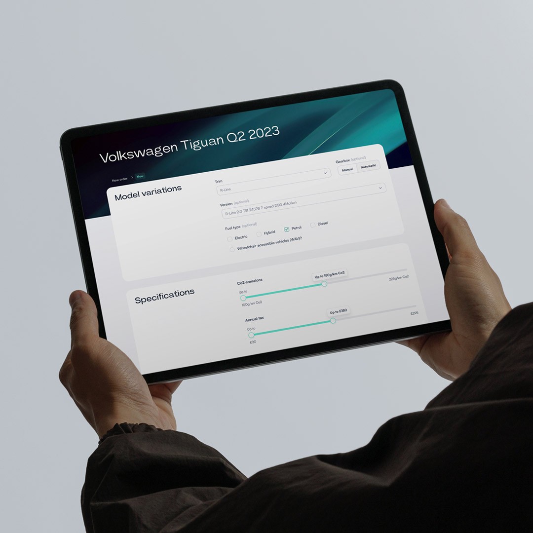 Hands holding tablet showing Orca vehicle configuration for Volkswagen Tiguan with model variations, fuel type, CO2 emissions and annual tax specification sliders