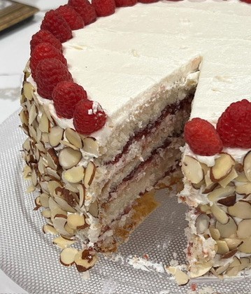 Slice of layered cake with white frosting and almond/rasberry decoration