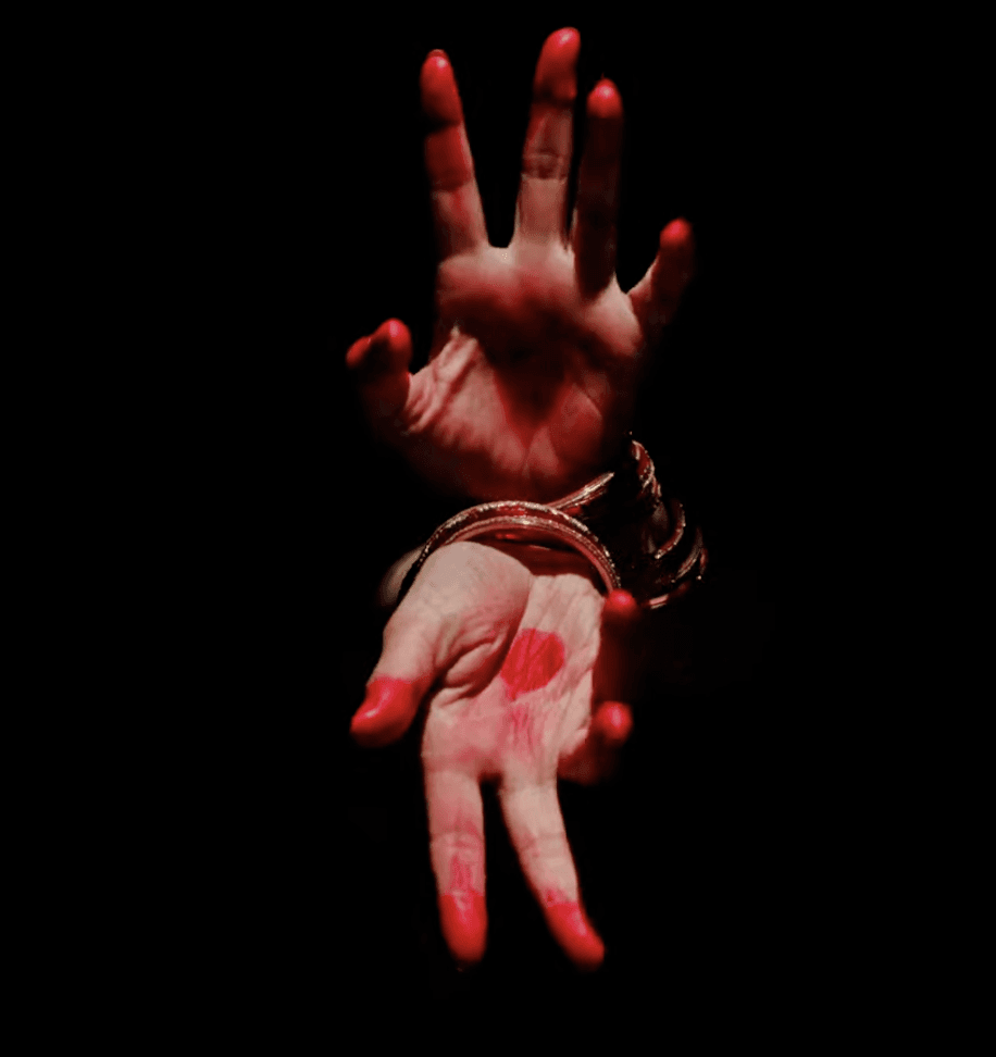Dramatic close-up of a woman’s outstretched hand wearing bangles, illuminated against a dark background.