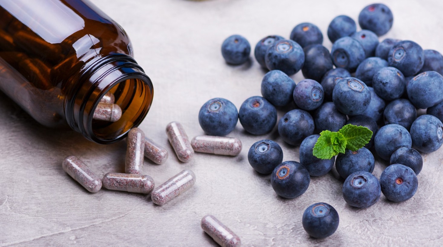 Supplement capsules spilling from a bottle beside blueberries