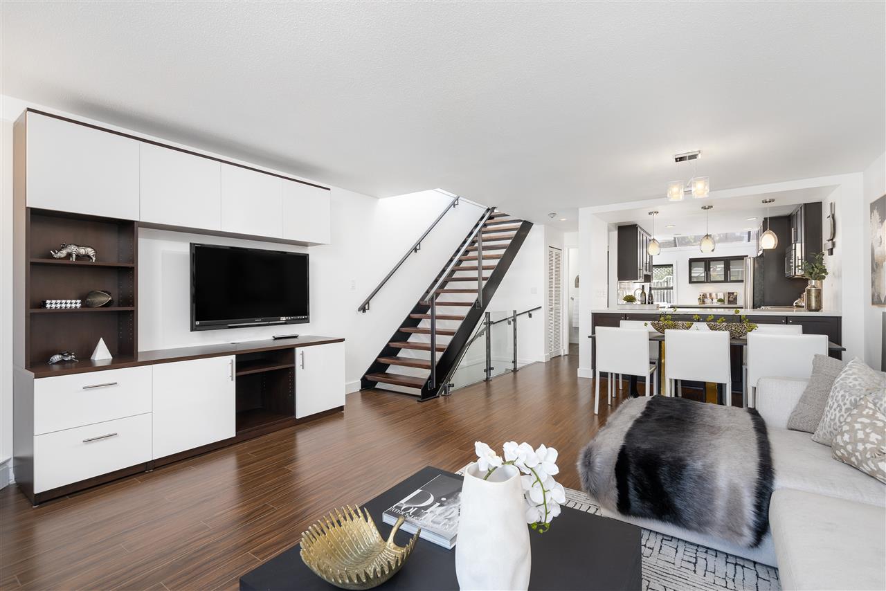 Modern open-concept living area featuring sleek furniture, a TV, and elegant decor under bright lighting.