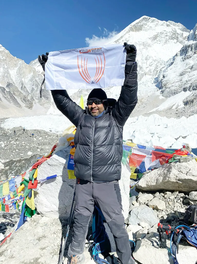Man standing on mountain peak, holding white flag with logo.