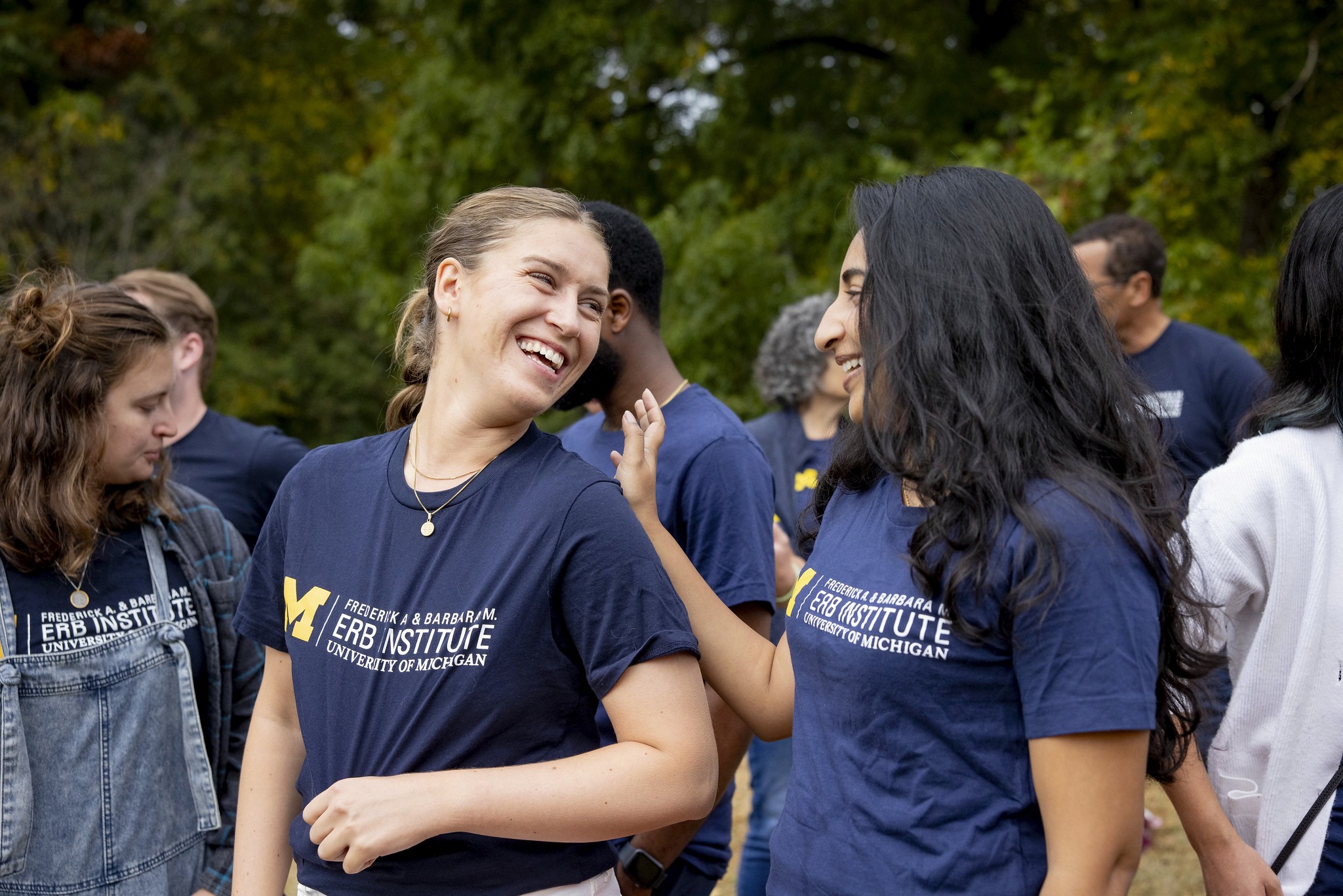 Two Erb students share a laugh outside. They both wear Erb branded t shirts and smile