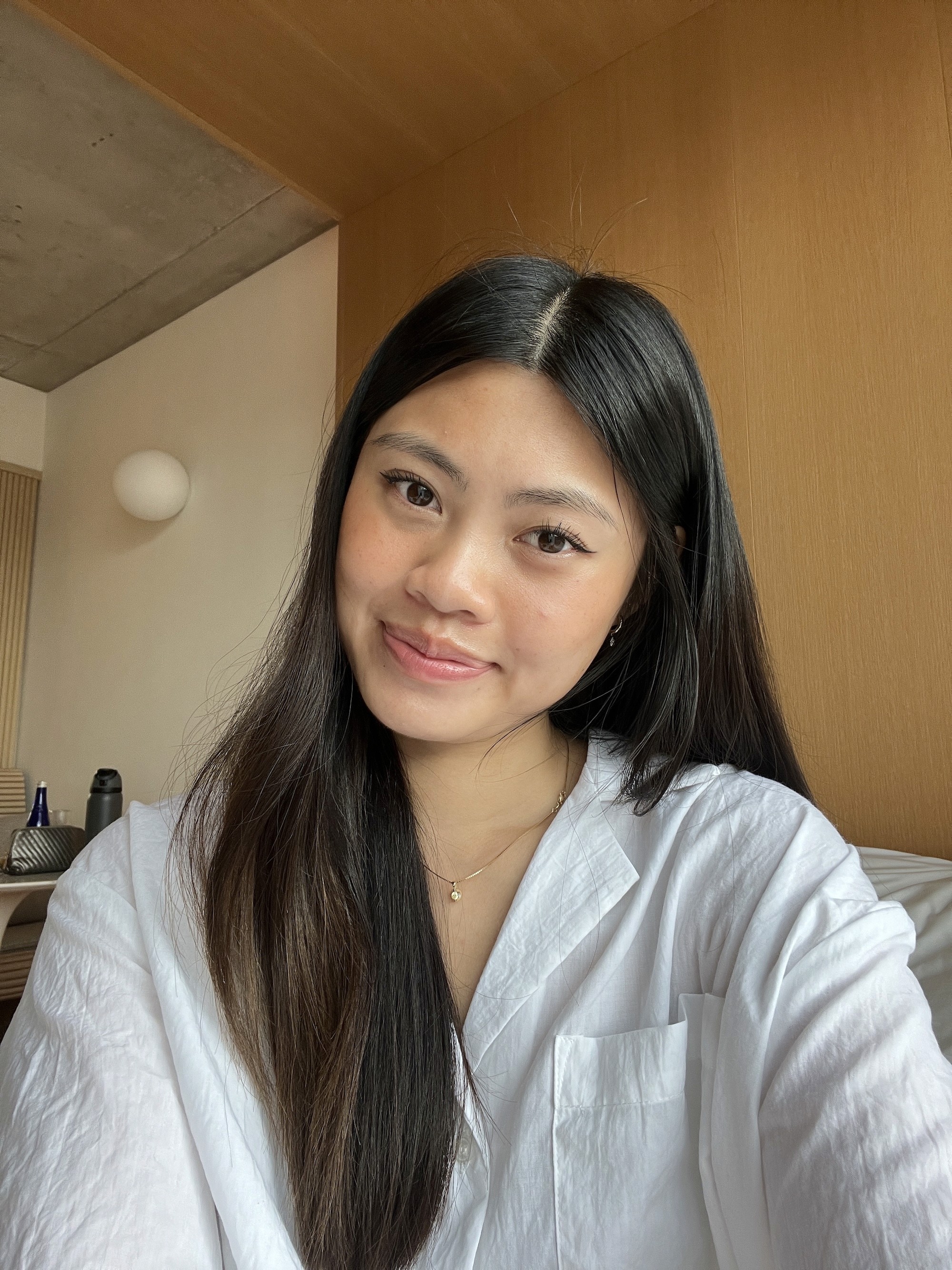 A photo of Misty Chung, and asian-american woman. She has long black hair, wearing a white button up, and is smiling at the camera.