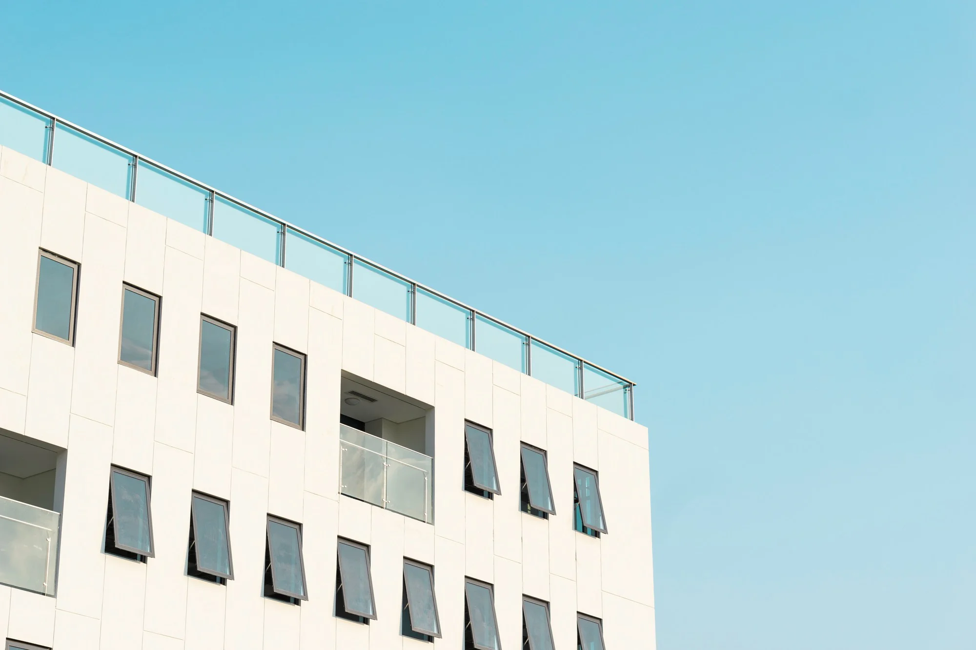 A white building with a balcony and windows, representing an apartment complex, set against a serene blue sky.