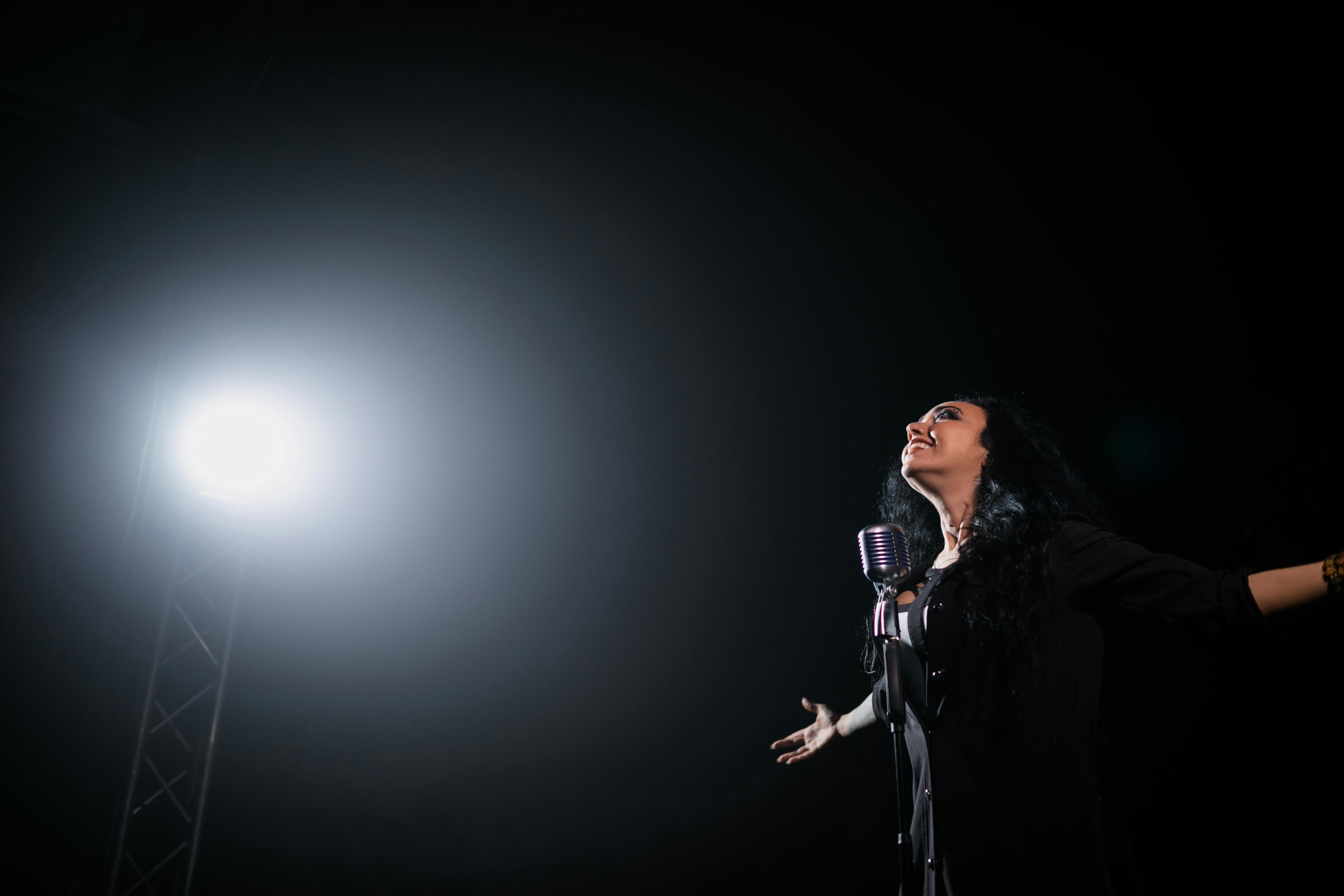 Woman singing on stage with spotlight and arms out