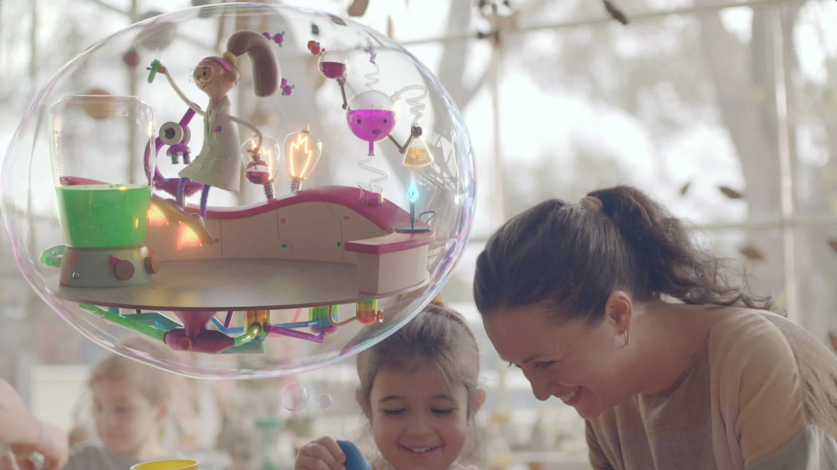 Woman and child laughing beside a floating bubble holding a science lab, from the Free Kinder Best Start, Best Life campaign