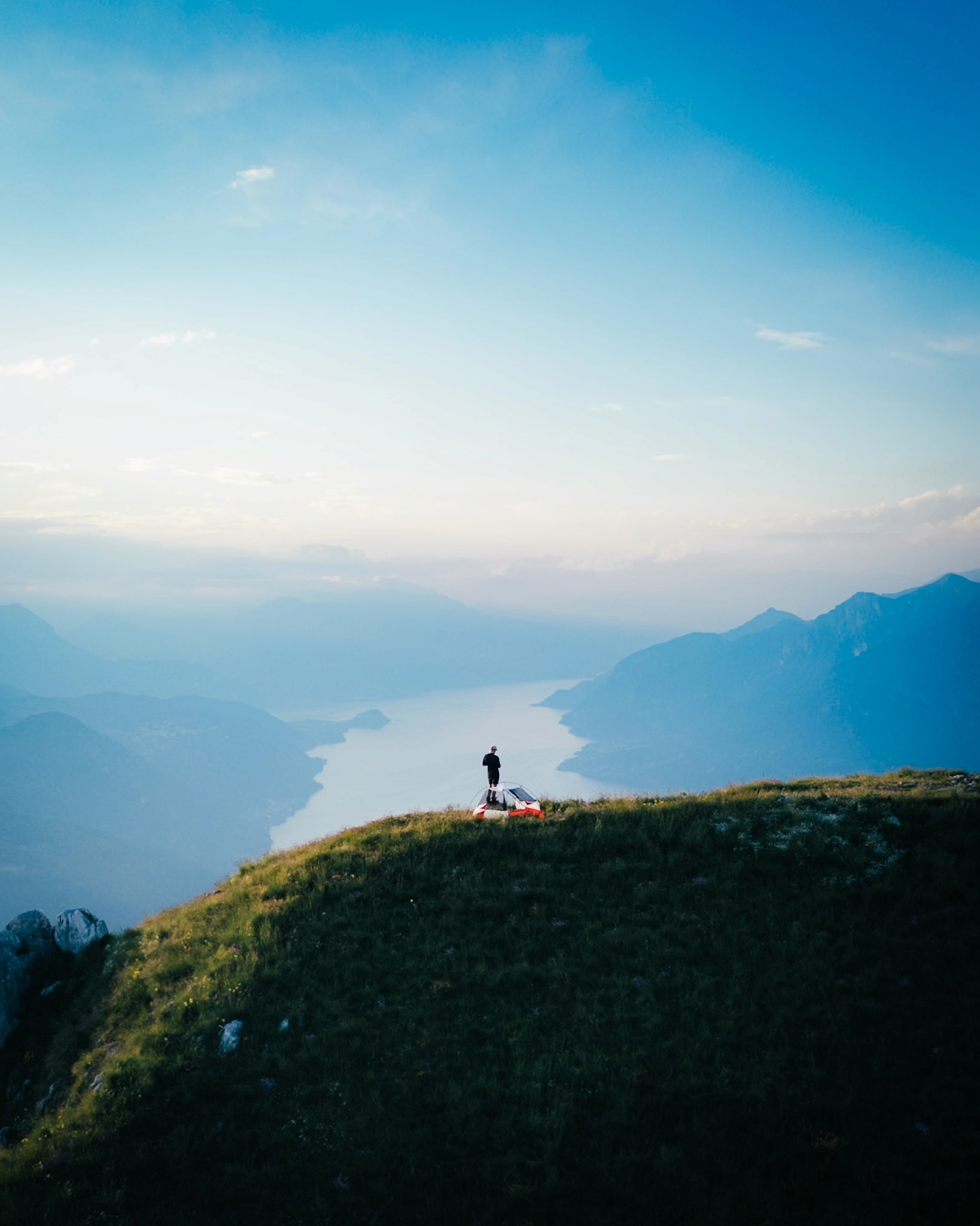 A person stands on a mountain peak, gazing at the panoramic landscape under a clear blue sky.
