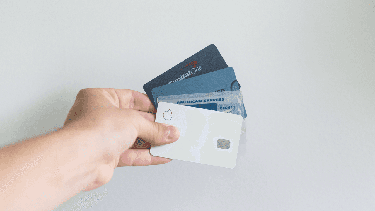 A hand outstretched holding for different credit cards against a white wall