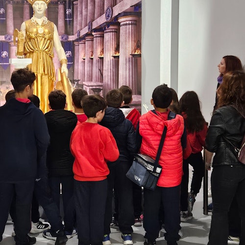 一群小朋友聚集在博物館內一座大型金色雕像四周。一名成人似乎正在講解這件展品。