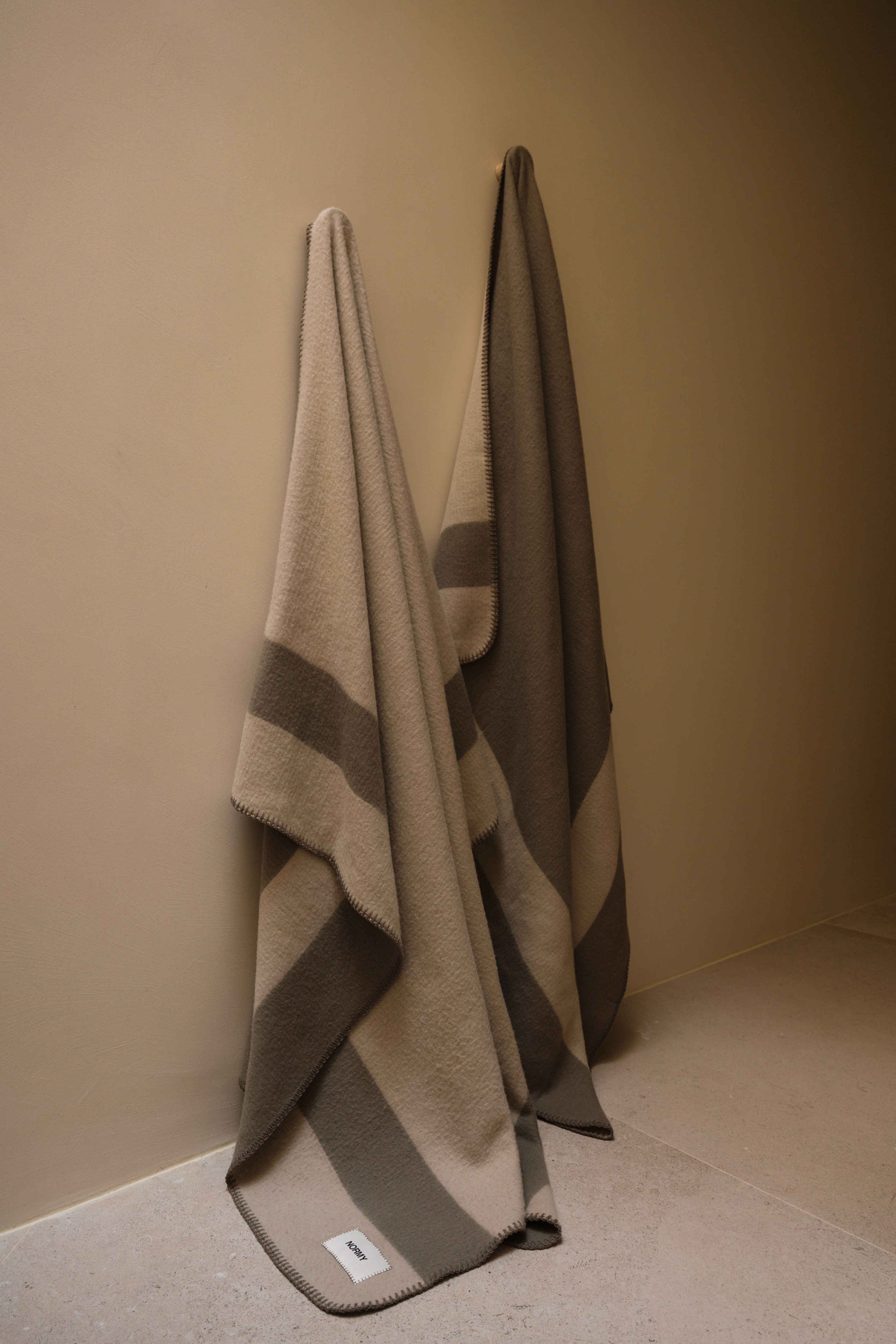 Striped beige and grey merino wool blankets hanging side by side against a beige wall
