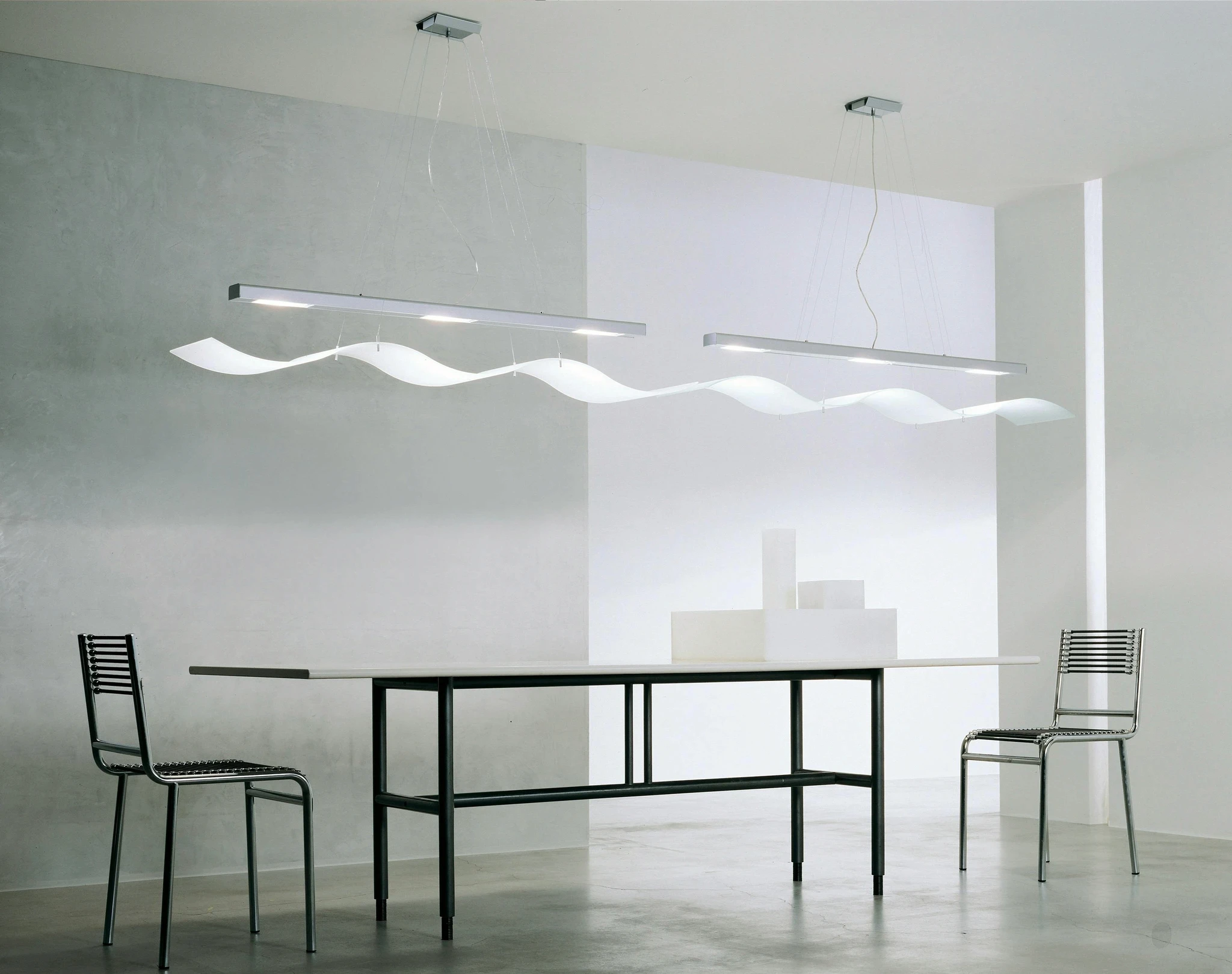 Minimalist interior design featuring a sleek black console table and a sculptural, wave-like pendant light in a bright, white studio.