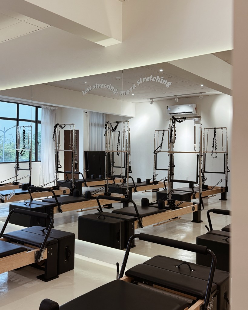 Interior of a Pilates studio featuring multiple reformer machines, large mirrors, and motivational text on the wall.