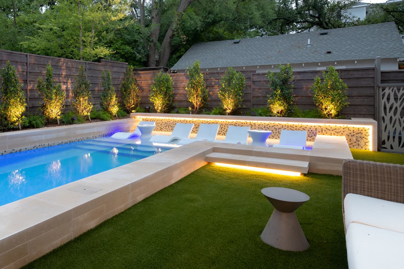Geometric pool design with built-in spa and LED lighting in Dallas luxury backyard featuring symmetrical plantings and modern hardscape