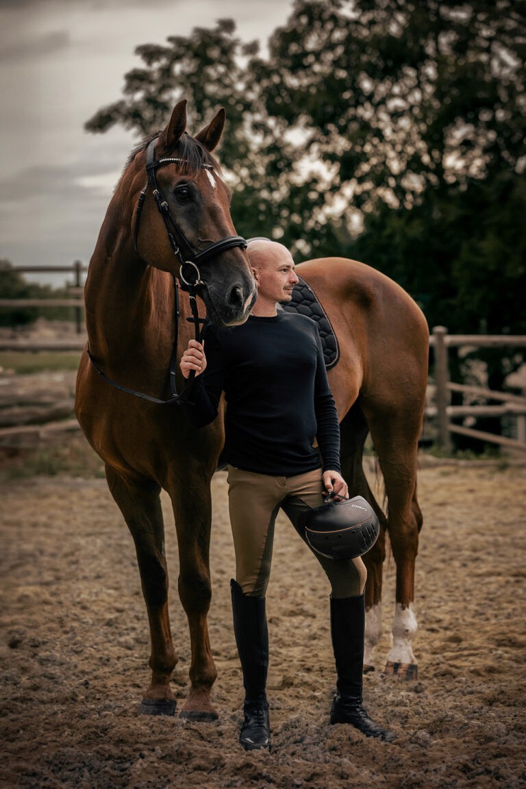 Philipp Reichart steht neben einem großen braunen Pferd mit englischer Ausrüstung und blickt in die Ferne.