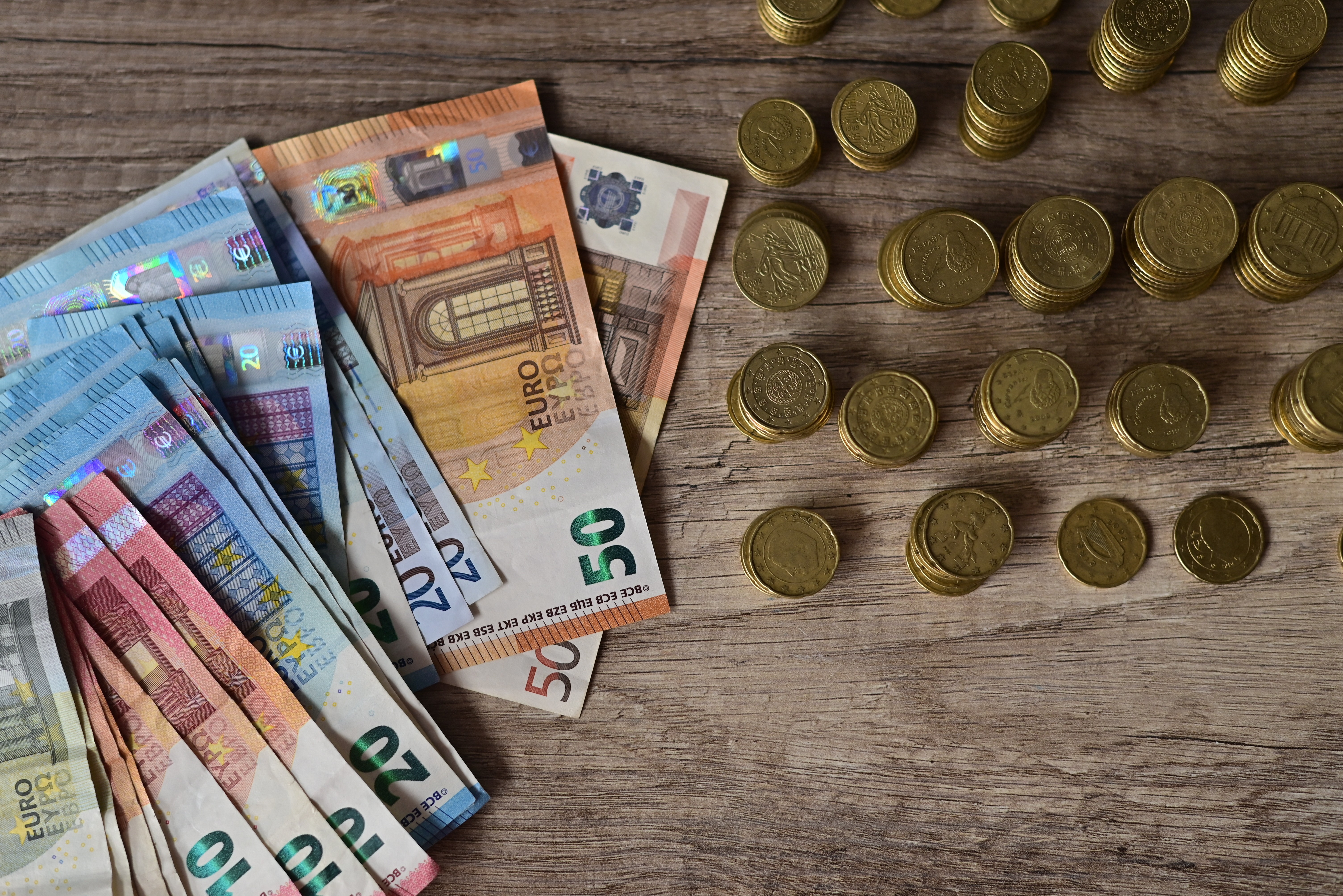 Euro banknotes and stacks of coins arranged on a wooden table.