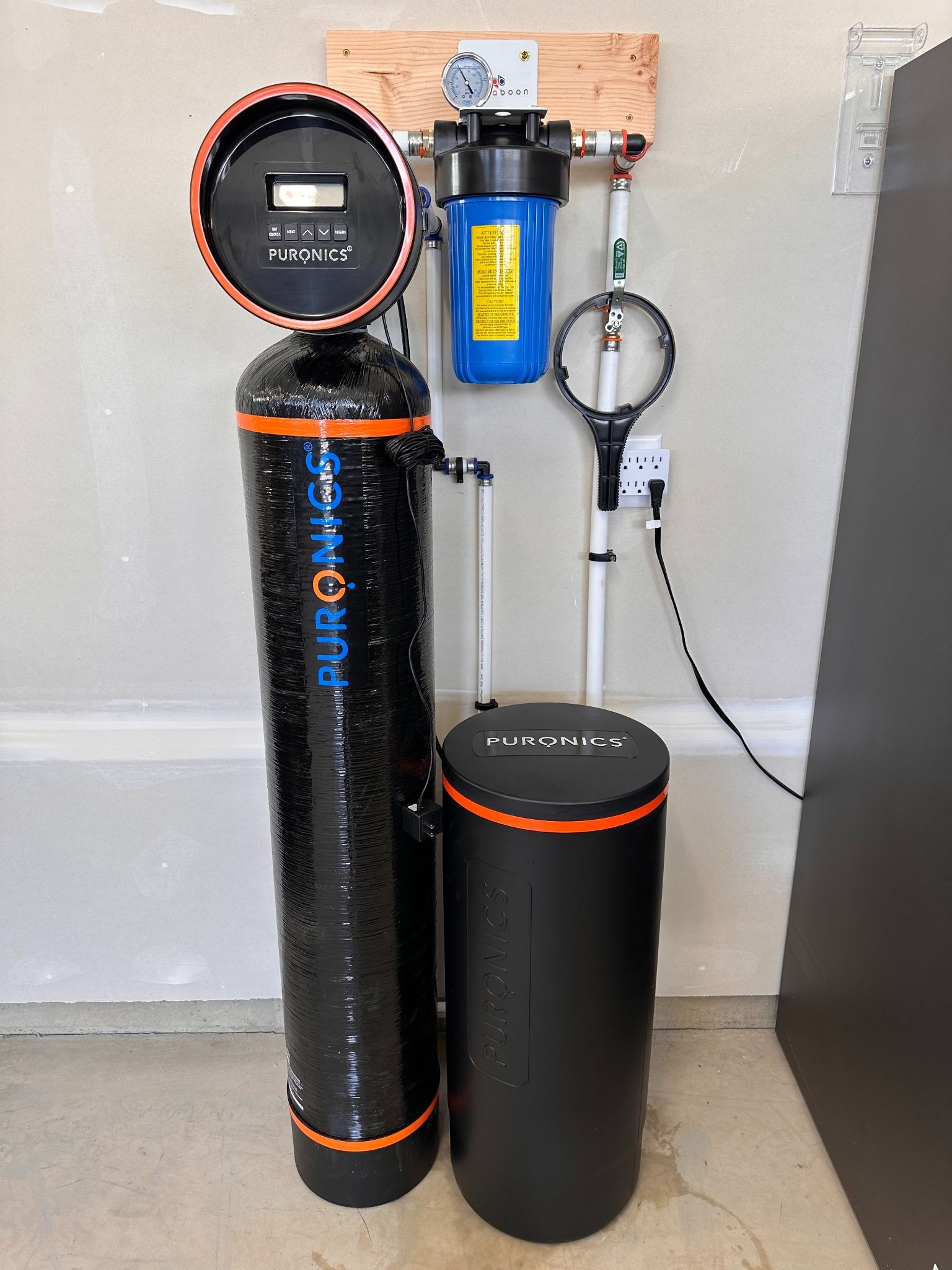 Puronics whole-house water treatment system with filtration tank, control unit, pressure gauge, and connected plumbing.