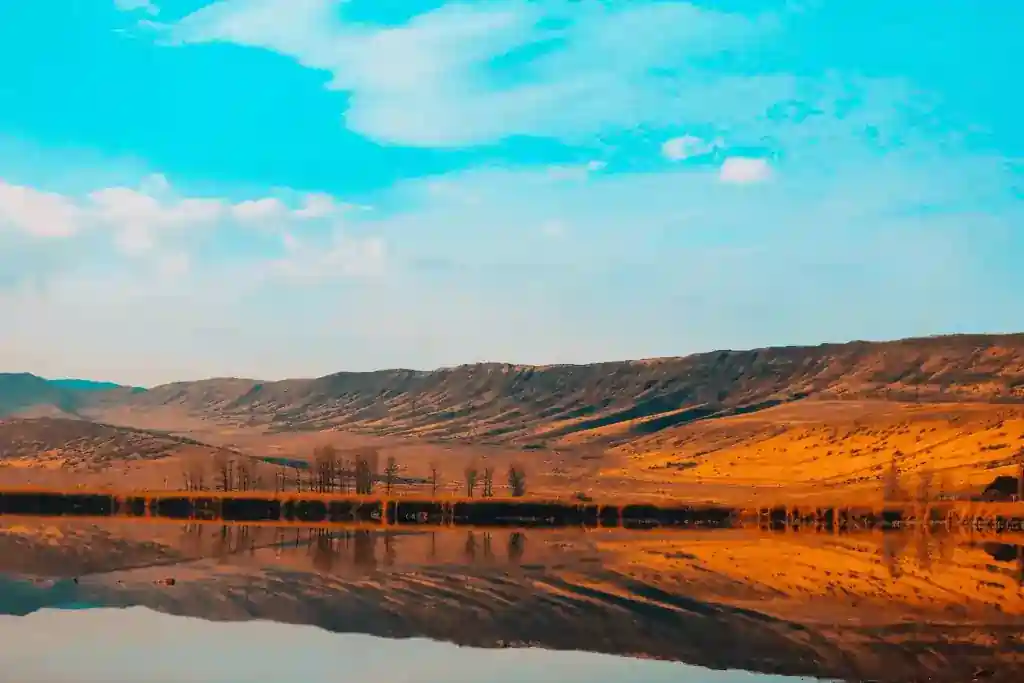 Golden hills reflect on a calm lake under a vivid blue sky.