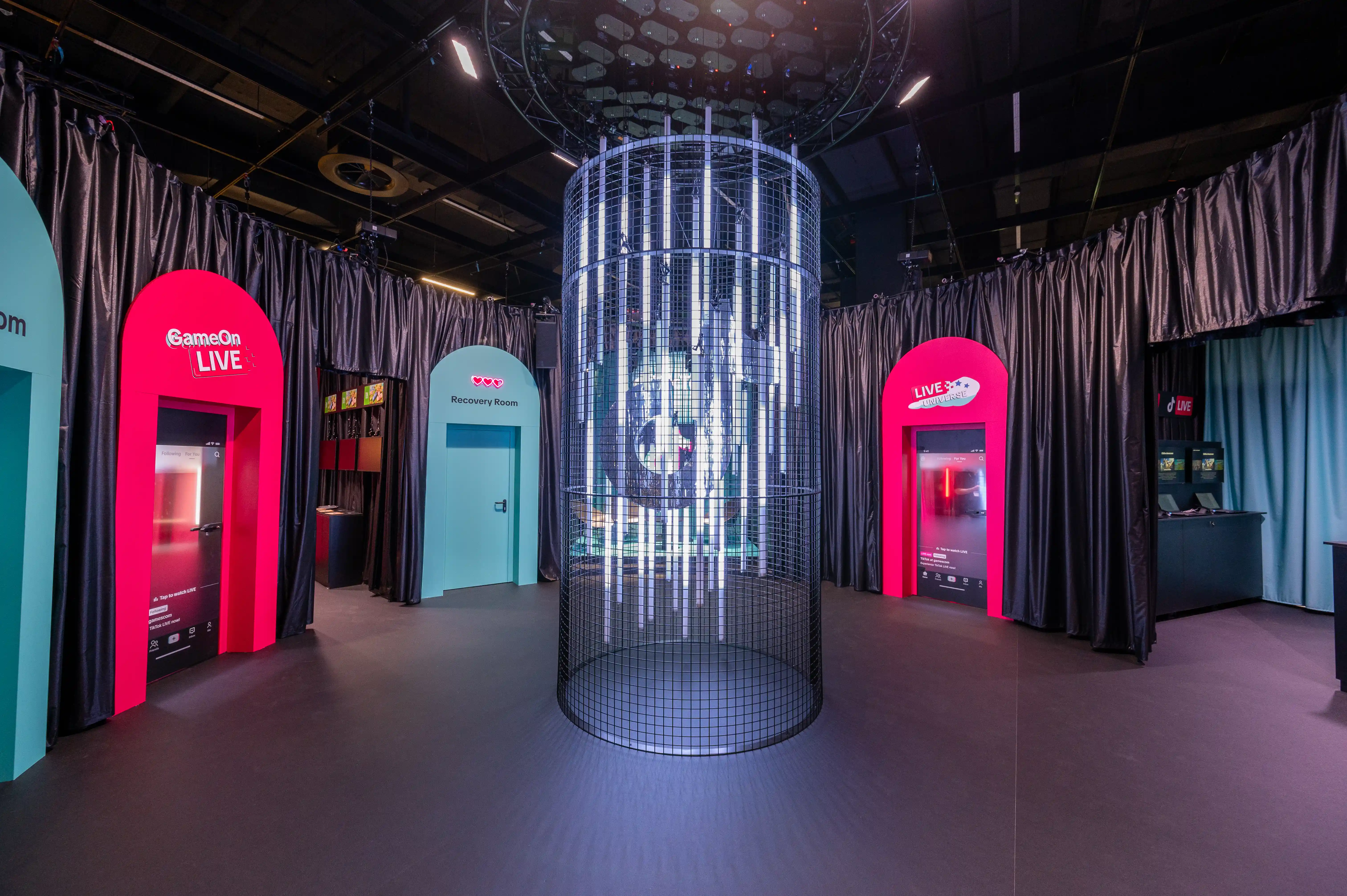Interior of the TikTok Gamescom booth with central light cylinder and arched portals to Live and Discovery rooms.