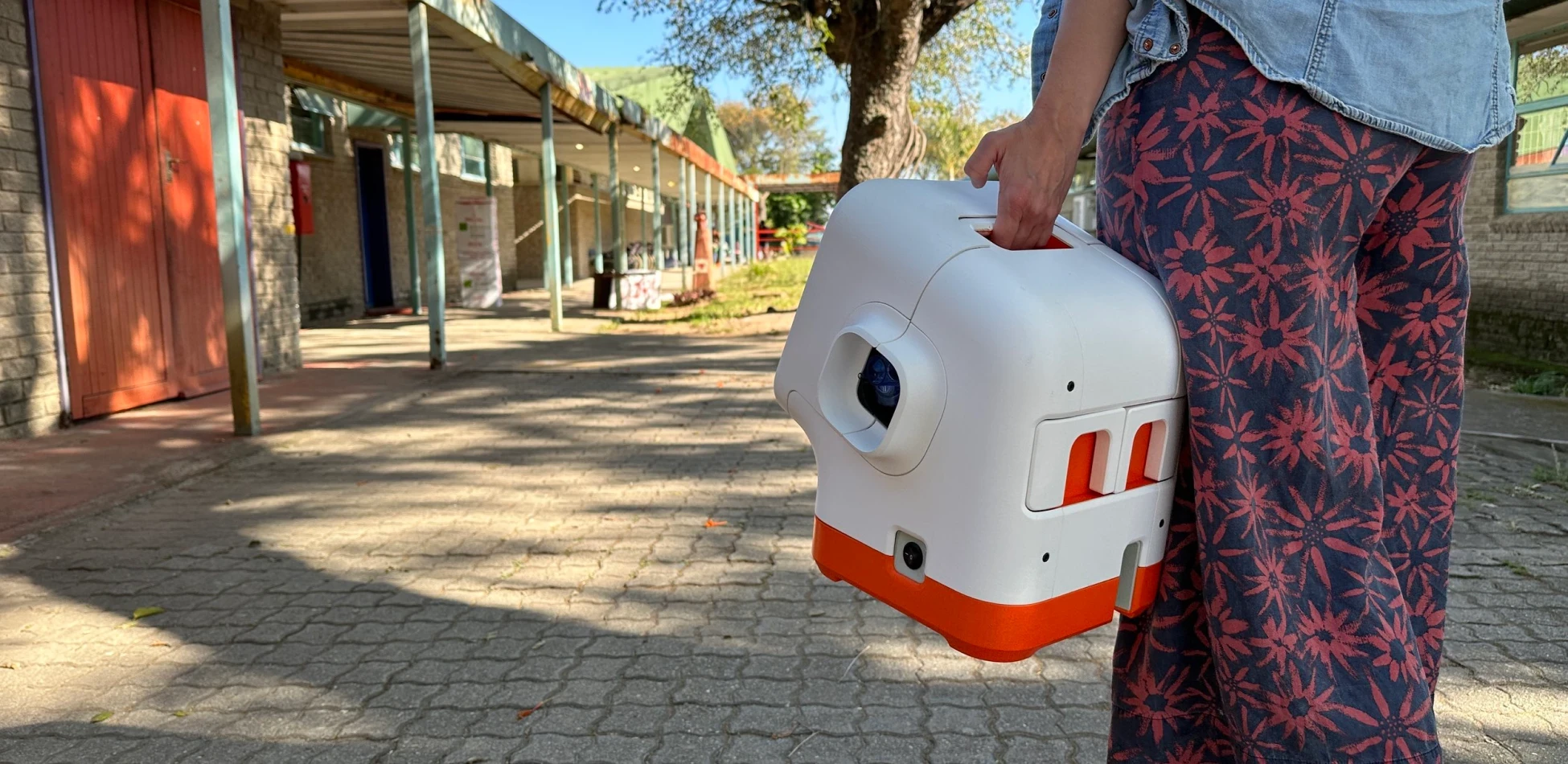 Person carrying innovative white and orange medical device along a walkway, showcasing portable healthcare technology in community setting.