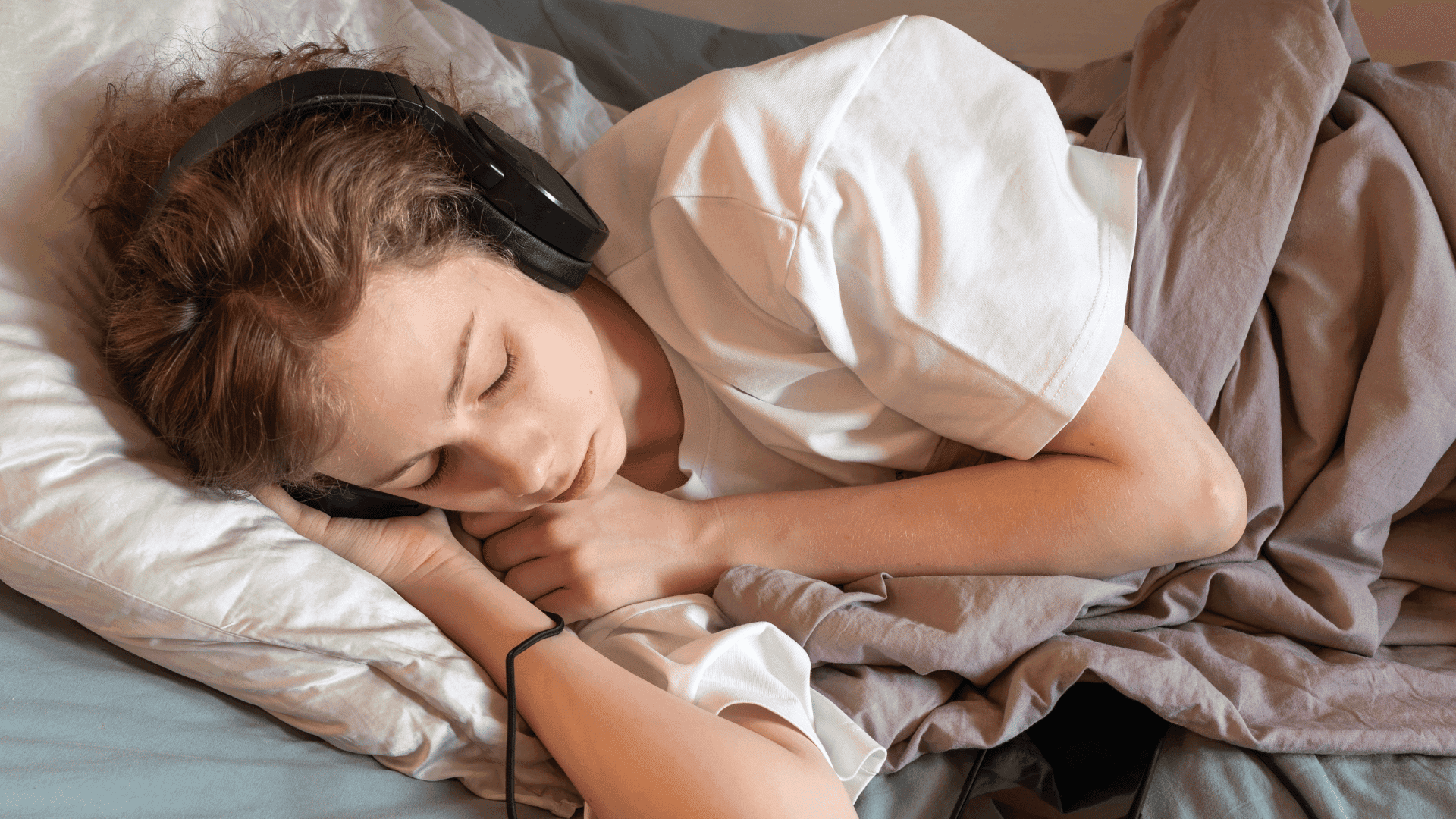 A child lying in bed with headphones on, eyes closed, visualising and imagining the sounds from HushAway®’s Sound Sanctuary.