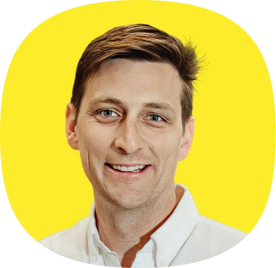 A smiling man with short brown hair wearing a white collared shirt, pictured in front of a bright yellow background.