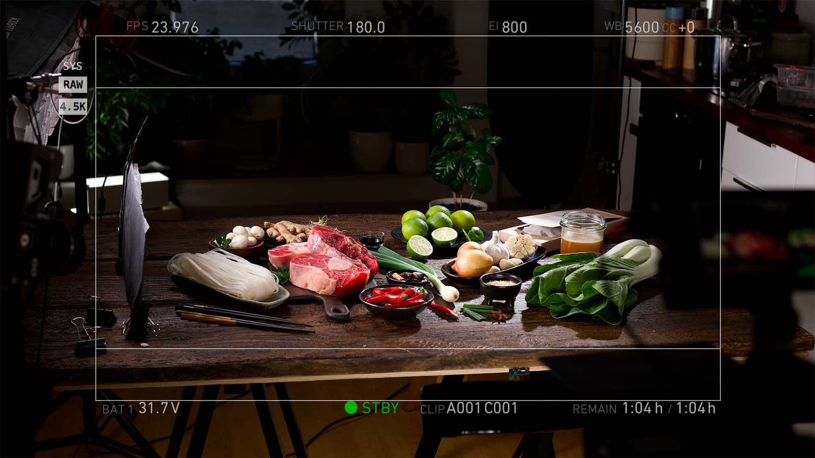 A wooden table in Abarel Studio displays fresh ingredients including beef, bok choy, limes, ginger, and peppers, captured through a preview monitor using an ARRI camera.
