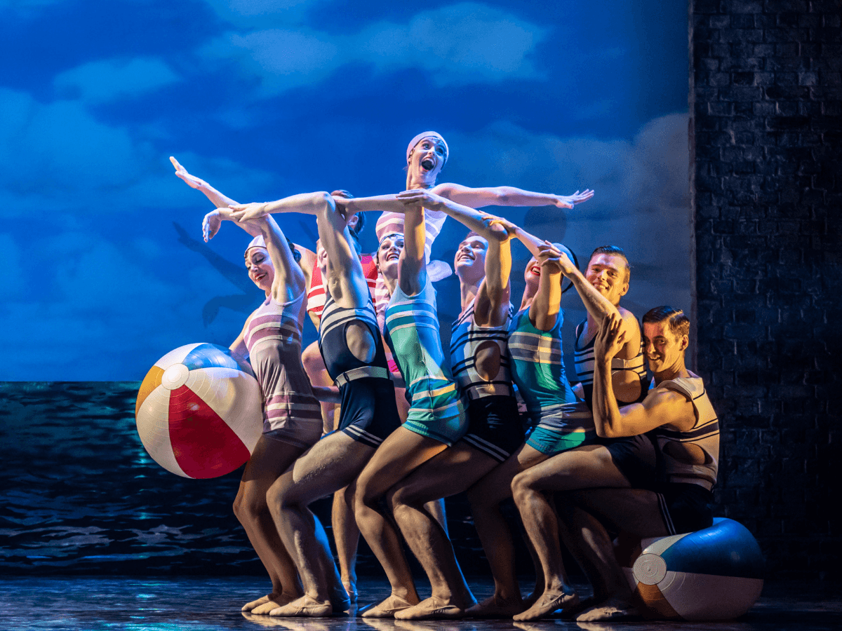 ビンテージ水着を着たモデルたちが青い海を背景にビーチボールを持ってポーズを決めています。