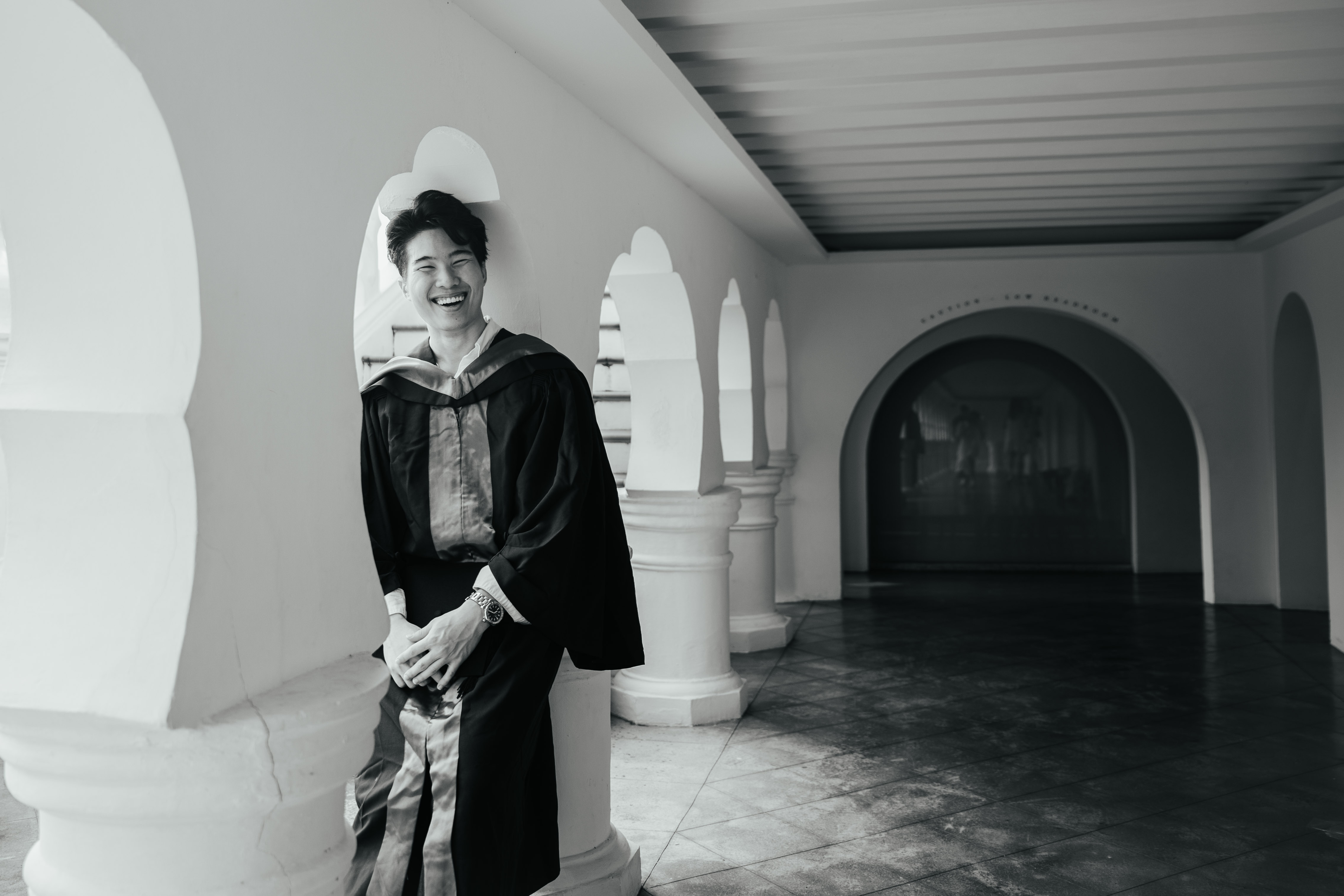 Candid shot of a young man laughing, leaning against a corridor in the Botanic Gardens.