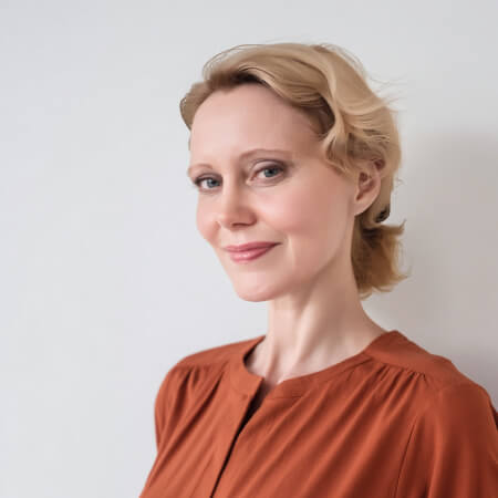 Side profile portrait of a woman with blonde hair pulled back, wearing a rust-colored blouse, smiling warmly