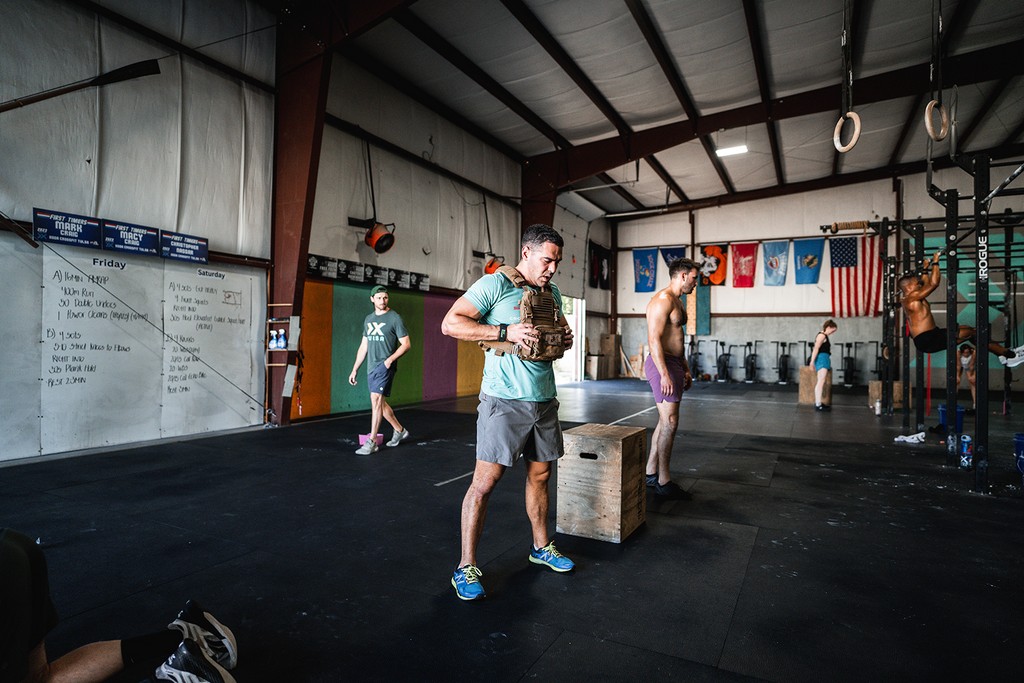 CrossFit athletes performing box jumps during a group workout inside an industrial-style gym.