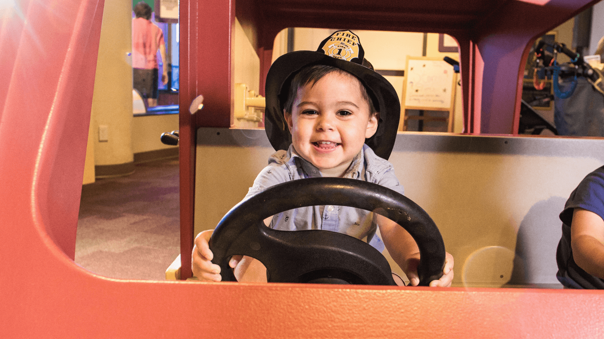 A young boy sits inside the toy fire truck pretending to be a firefighter.