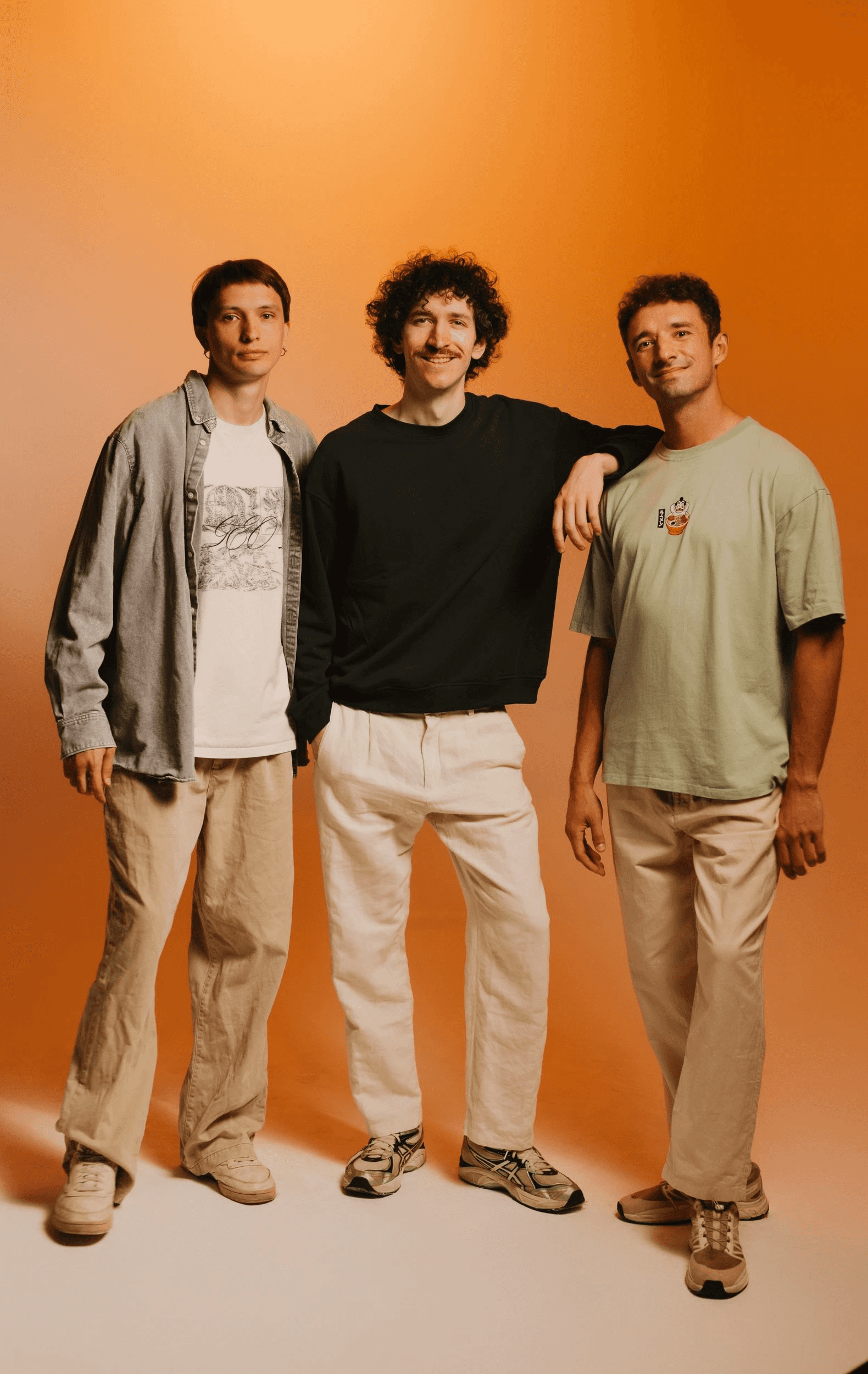 Sergey, Borys, and Ilja in a studio portrait on a warm orange background.